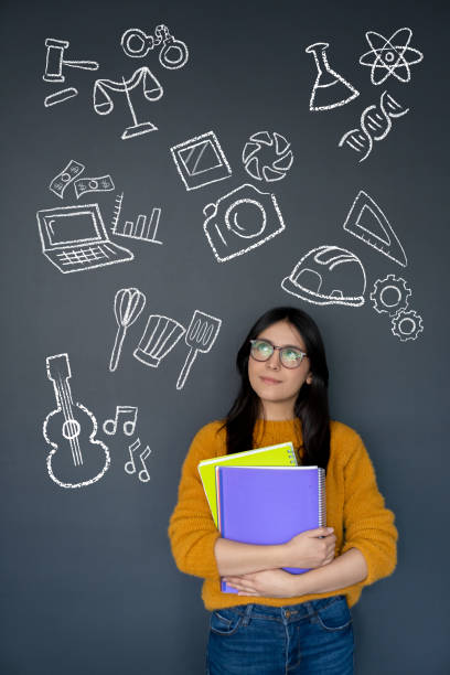 Happy student thinking about what to study as her major and looking at the options on a blackboard â education concepts