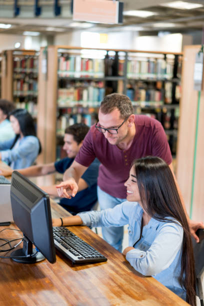 Teacher helping female student with their research on the computer at the library - education concepts